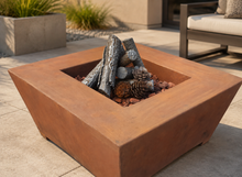 Load image into Gallery viewer, A square, open-top fire pit table with a warm rust-brown finish, shown outdoors on a patio with faux logs and pinecones inside.
